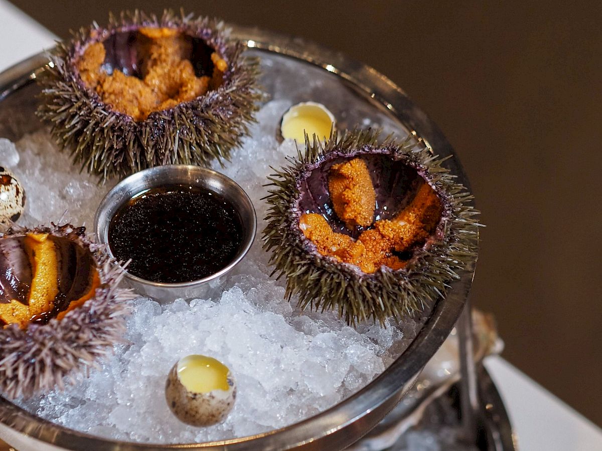 The image shows a seafood platter with sea urchins, oysters, and lemon wedges on ice, arranged on a two-tiered stand.