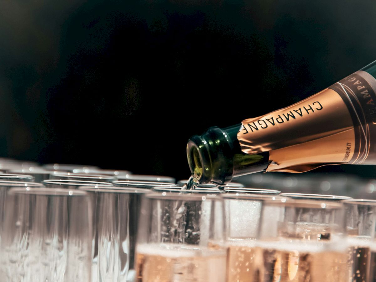 A bottle of champagne is being poured into a row of glasses, suggesting a celebratory event or gathering.